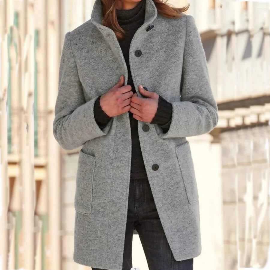 Woman wearing a longline single breasted coat with stand collar and two front patch pockets over a roll neck and jeans._0
