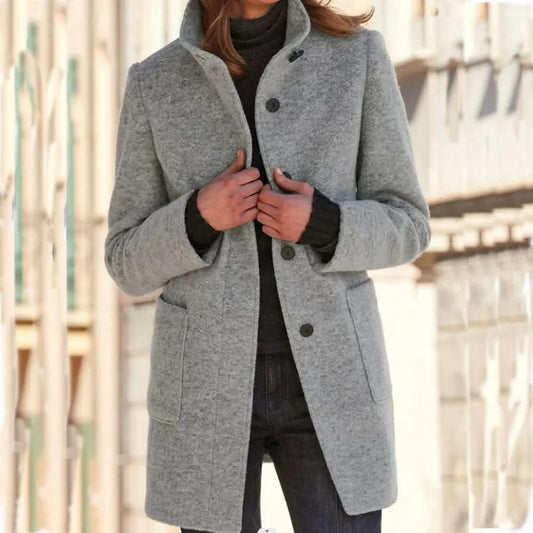 Woman wearing a longline single breasted coat with stand collar and two front patch pockets over a roll neck and jeans._0